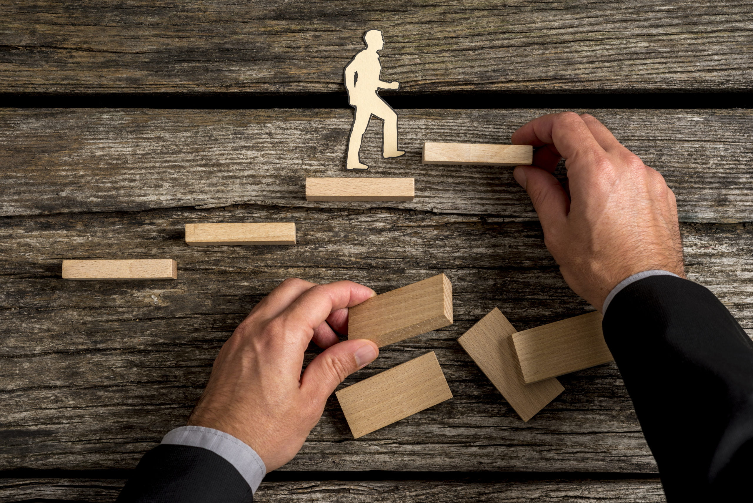 Conceptual image of personal and career promotion Silhouette cutouts of a man walking up steps, while the hand of other businessman building stairs for him in a conceptual image of personal and career promotion.