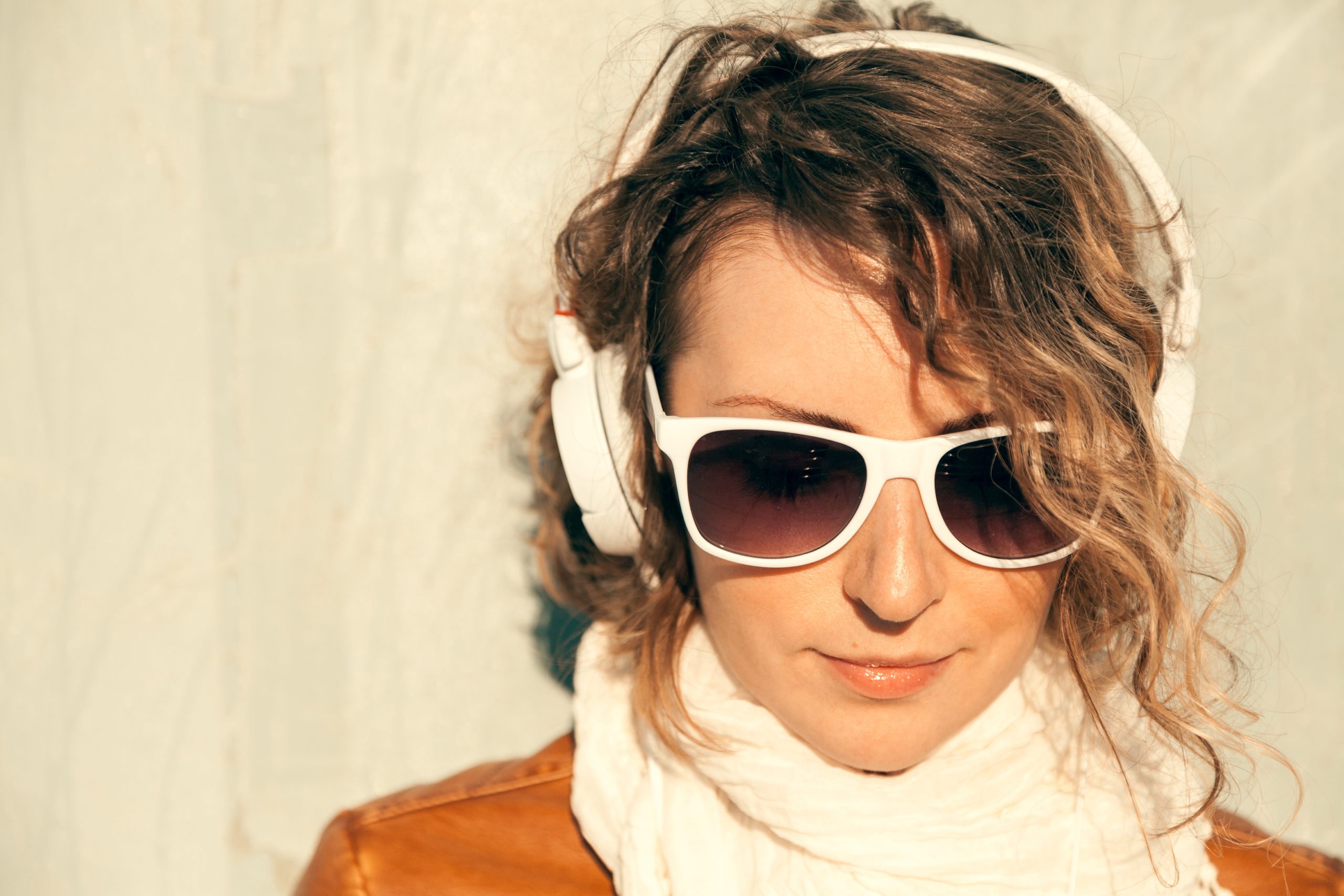 Beautiful young woman in a sunglasses and headphones listening music near the wall